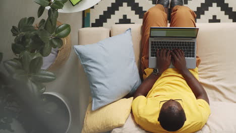 Afro-American-Man-Sitting-on-Sofa-and-Typing-on-Laptop